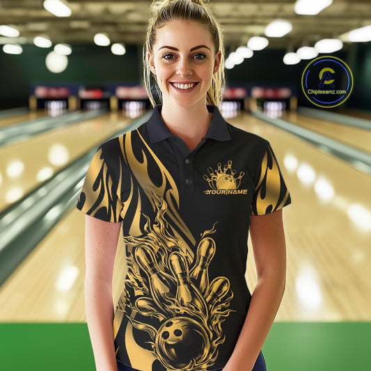 Female model front view at a bowling lane wearing a black polo shirt showcasing a golden metal tribal flame bowling ball striking pins in a powerful action scene.