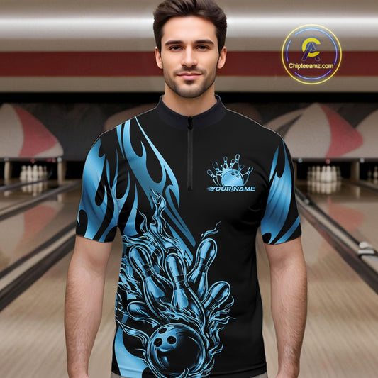 Male model front view inside bowling center wearing black quarter zip with blue gradient tribal flame bowling ball hitting pins in energetic action scene.