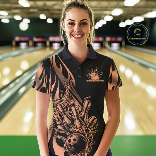 Female model front view at bowling lane wearing black polo shirt with rose gold tribal flame bowling ball hitting pins in dynamic sports action scene.
