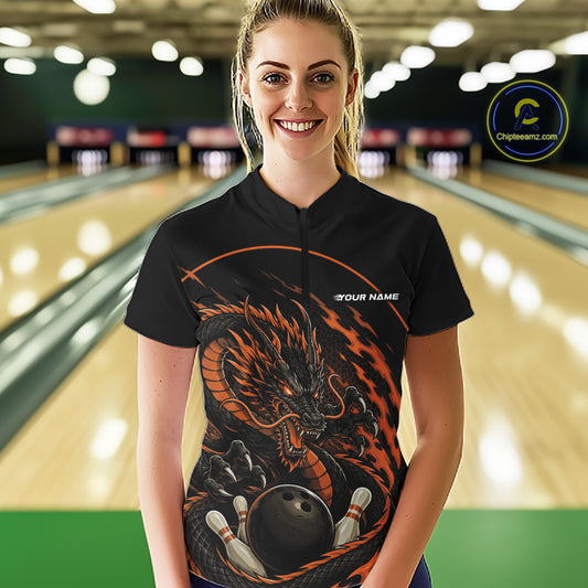 Front view of a happy female model in a bowling alley wearing an orange custom quarter-zip bowling shirt featuring an aggressive dragon with flames in a dynamic and energetic design.