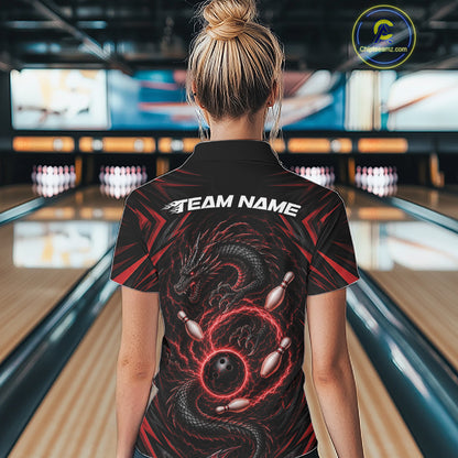 A woman viewed from behind wearing a black bowling-themed short-sleeve quarter zip shirt with a red and black dragon graphic and white 'TEAM NAME' text on the back, standing in a bowling alley.
