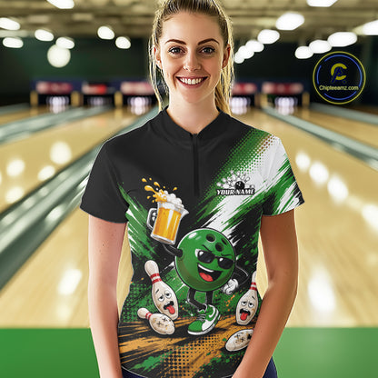 A woman stands in a bowling alley wearing a custom short-sleeve quarter zip shirt with a green and black bowling-themed graphic print featuring a funny cartoon bowling ball with a beer pitcher and pins. 