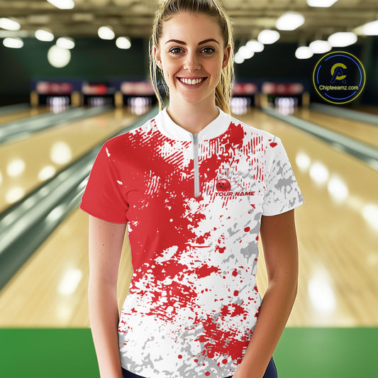 Front view of a female model in a bowling lane wearing a red and white splatter bowling quarter-zip shirt with bold athletic bowling graphics.