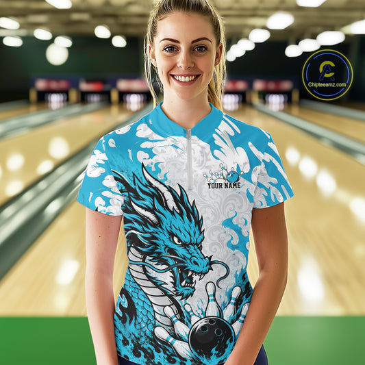 Woman wearing a blue and white dragon-themed bowling shirt in a bowling alley.