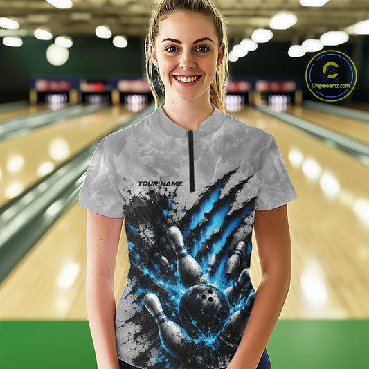 Front view of a female model wearing a gray bowling quarter zip shirt featuring a dramatic blue bowling ball and pins graphic with claw-mark artwork in a bowling lane.