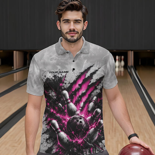 Front view of a male model wearing a gray bowling polo shirt featuring a dramatic pink bowling ball striking pins graphic with claw-mark artwork at a bowling lane.