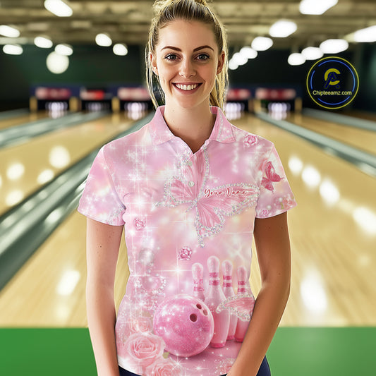 Female model in a bowling venue wearing a bowling polo shirt with sparkling butterfly artwork, diamond accents, bowling pins, and a bowling ball.