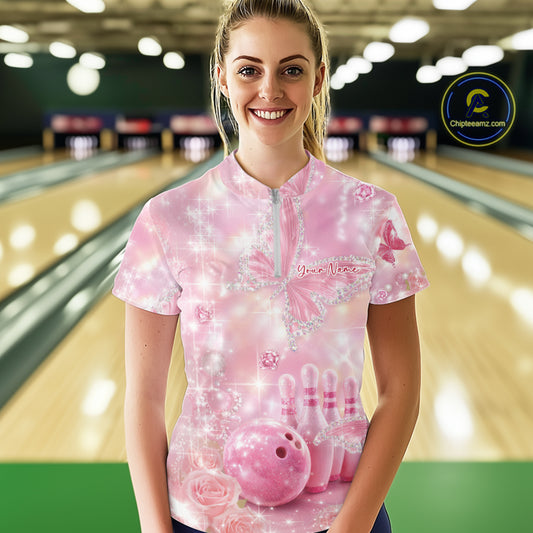 Front view of a female model in a bowling venue wearing a quarter-zip shirt adorned with glitter butterflies, diamond accents, and bowling-themed artwork.