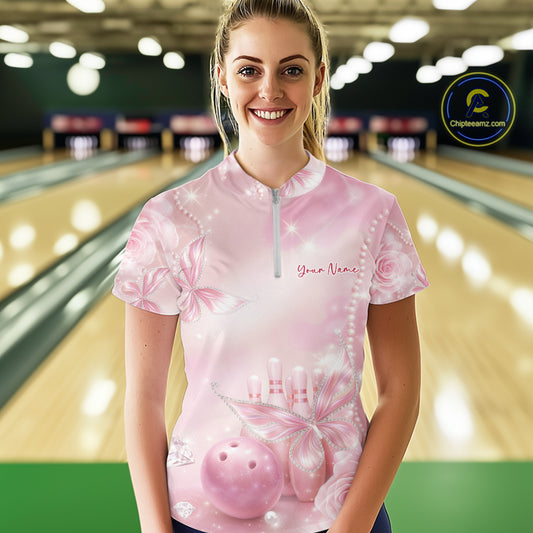Front view of a female model wearing a bowling quarter-zip shirt at the lane with glitter butterfly motifs, diamonds, bowling pins, and a bowling ball.