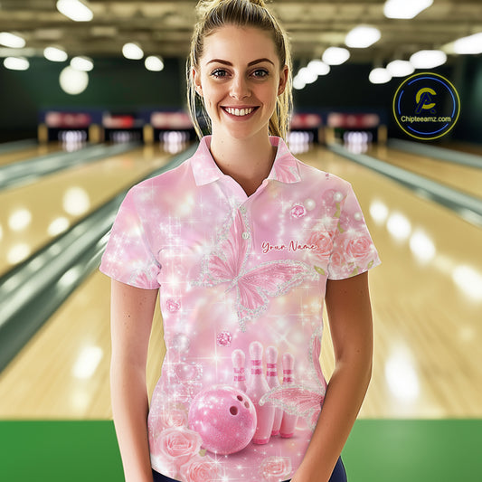 Female model at a bowling lane wearing a bowling polo shirt with glitter butterfly artwork, diamond accents, bowling pins, and a bowling ball.