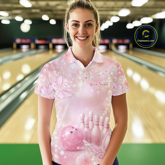 Female model in a bowling center wearing a bowling polo shirt with glitter butterfly accents, roses, bowling pins, and a bowling ball illustration.