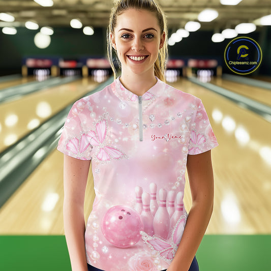 Female model wearing a quarter-zip bowling shirt in a bowling alley with pink glitter butterflies, floral roses, bowling pins, and bowling ball artwork.