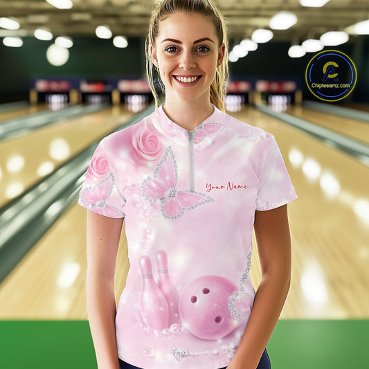 Female model wearing a bowling quarter-zip shirt at the bowling lane with pink glitter butterfly artwork, roses, bowling pins, and a bowling ball on the front.