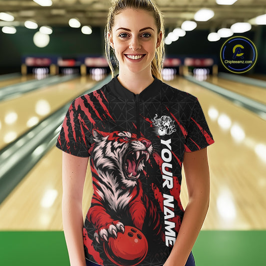Front view of a female model in a bowling lane wearing a black and red bowling quarter-zip shirt showcasing a roaring tiger holding a red bowling ball with matching red claw-stripe artwork and a geometric background pattern.