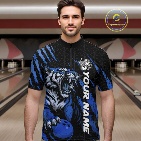 Male model wearing a black and mid blue bowling quarter-zip shirt in a bowling lane, displaying a roaring tiger holding a mid blue bowling ball with coordinated claw-stripe graphics and a geometric background pattern.