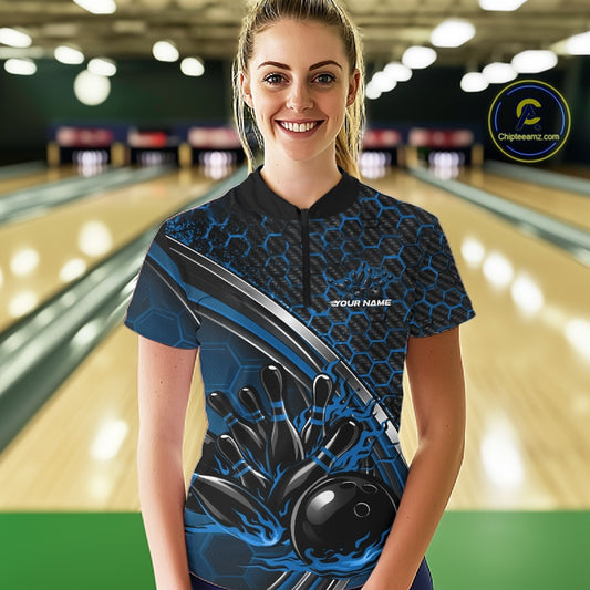 Female model wearing a black and blue bowling quarter zip with honeycomb accents and flaming bowling ball knocking down pins artwork at the bowling lane.