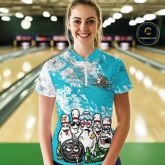 Front view of a female model in a bowling lane wearing a white quarter-zip shirt with turquoise blue and white grunge splatter design and playful bowling-themed illustration.