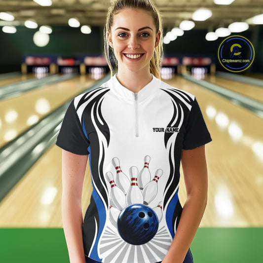 Female model wearing a white, black, and blue bowling quarter zip shirt featuring bowling ball and pins graphics, shown from the front at a bowling lane.