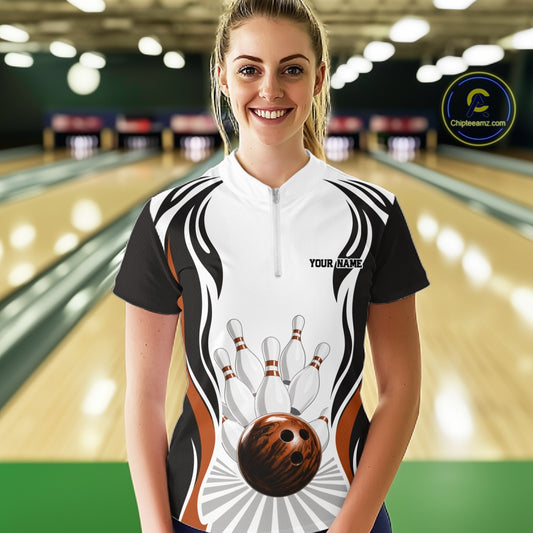 Front view of a female model in a bowling venue wearing a white, black, and orange bowling quarter-zip shirt featuring bowling-themed graphics with a bowling ball and pins.