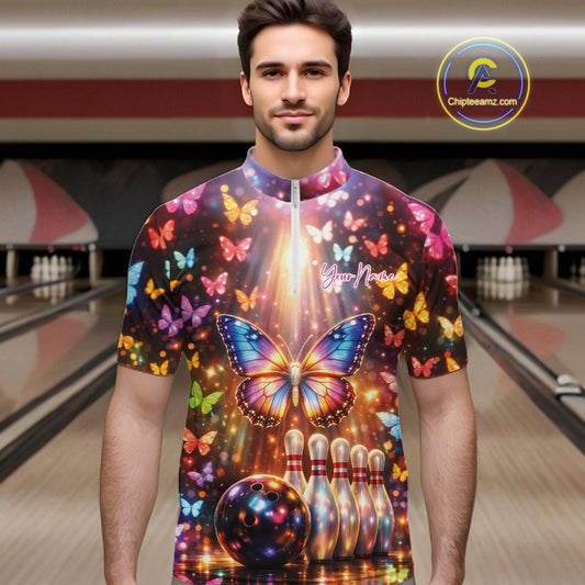 Male model at a bowling lane wearing a bowling quarter-zip shirt with colorful butterfly artwork, bowling pins, a bowling ball, and sparkling accents.
