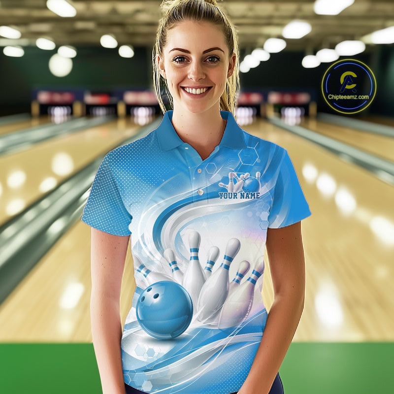 Female model standing in a bowling lane wearing a white and blue bowling polo shirt featuring abstract wave lines and a glossy bowling ball striking pins on the front.