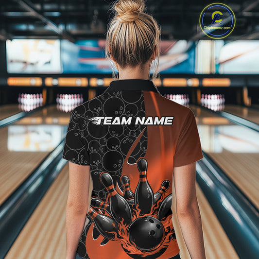 Back view of a female model in a bowling lane wearing a black and orange polo shirt with flaming black bowling ball striking pins and dynamic bowling visuals.