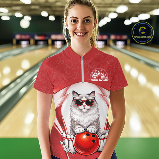 Female model shown from the front in a bowling venue wearing a quarter-zip shirt with a ragdoll cat in sunglasses and bowling ball artwork.