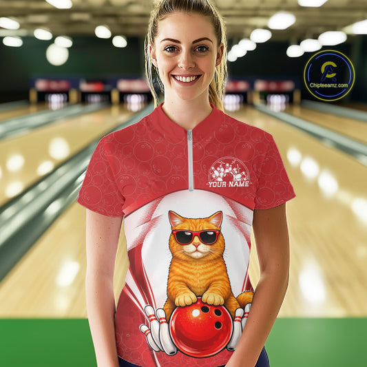 Female model wearing a white and red bowling quarter-zip shirt at a bowling lane with an orange British Shorthair cat in sunglasses beside a bowling ball.