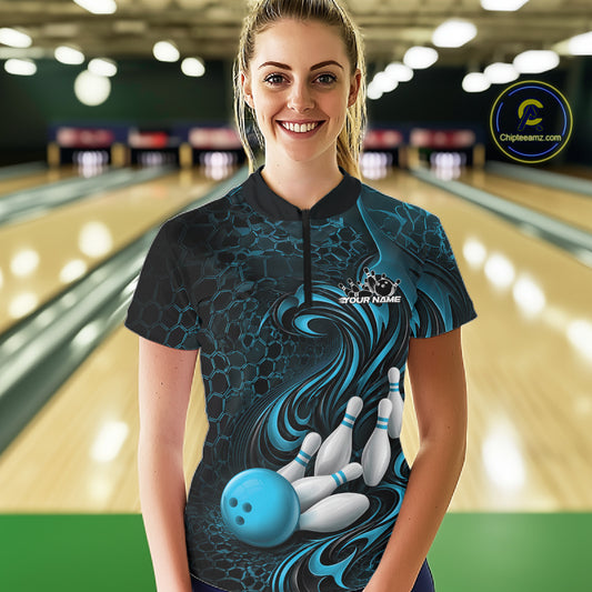 Female model standing in a bowling lane wearing a black and blue bowling quarter-zip shirt featuring a tribal flame bowling ball and pins graphic on the front.