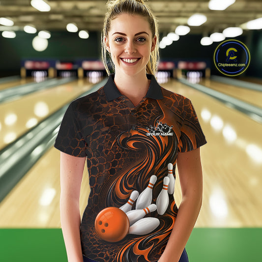 Female model standing in a bowling lane wearing a black and orange bowling polo shirt featuring a tribal flame bowling ball and pins graphic on the front.