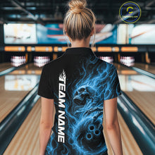 Load image into Gallery viewer, Back view of a female model wearing a black bowling polo shirt in a bowling alley featuring a skull clutching a bowling ball surrounded by swirling blue energy flames