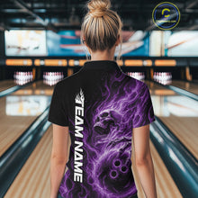 Load image into Gallery viewer, Back view of a female model wearing a black bowling polo shirt in a bowling alley featuring a skull clutching a bowling ball with swirling purple energy flames
