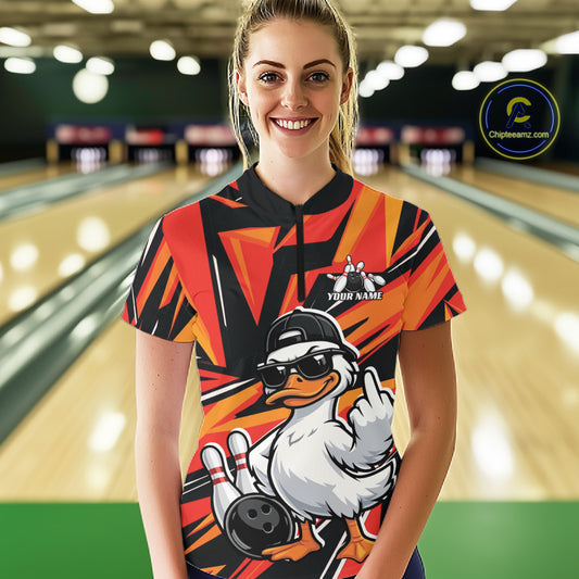 Female model in a bowling center wearing a black and orange quarter-zip with duck-themed bowling artwork and geometric accents.