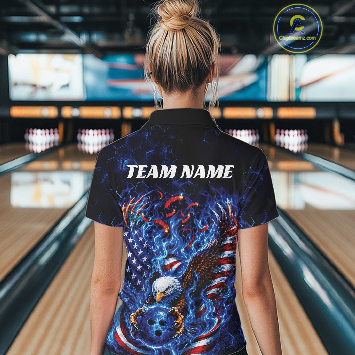 Back view of a female model in a bowling lane wearing a quarter zip shirt with flaming bald eagle, blue bowling ball, American flag, and blue flames.