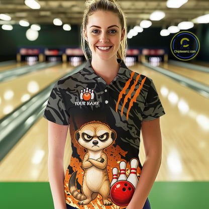 A woman stands in a bowling alley wearing a short-sleeve polo shirt with a black and gray tiger-stripe pattern, orange claw marks, a cartoon meerkat, bowling pins, and a red bowling ball graphic. The shirt also has a white 'YOUR NAME' placeholder on the chest.