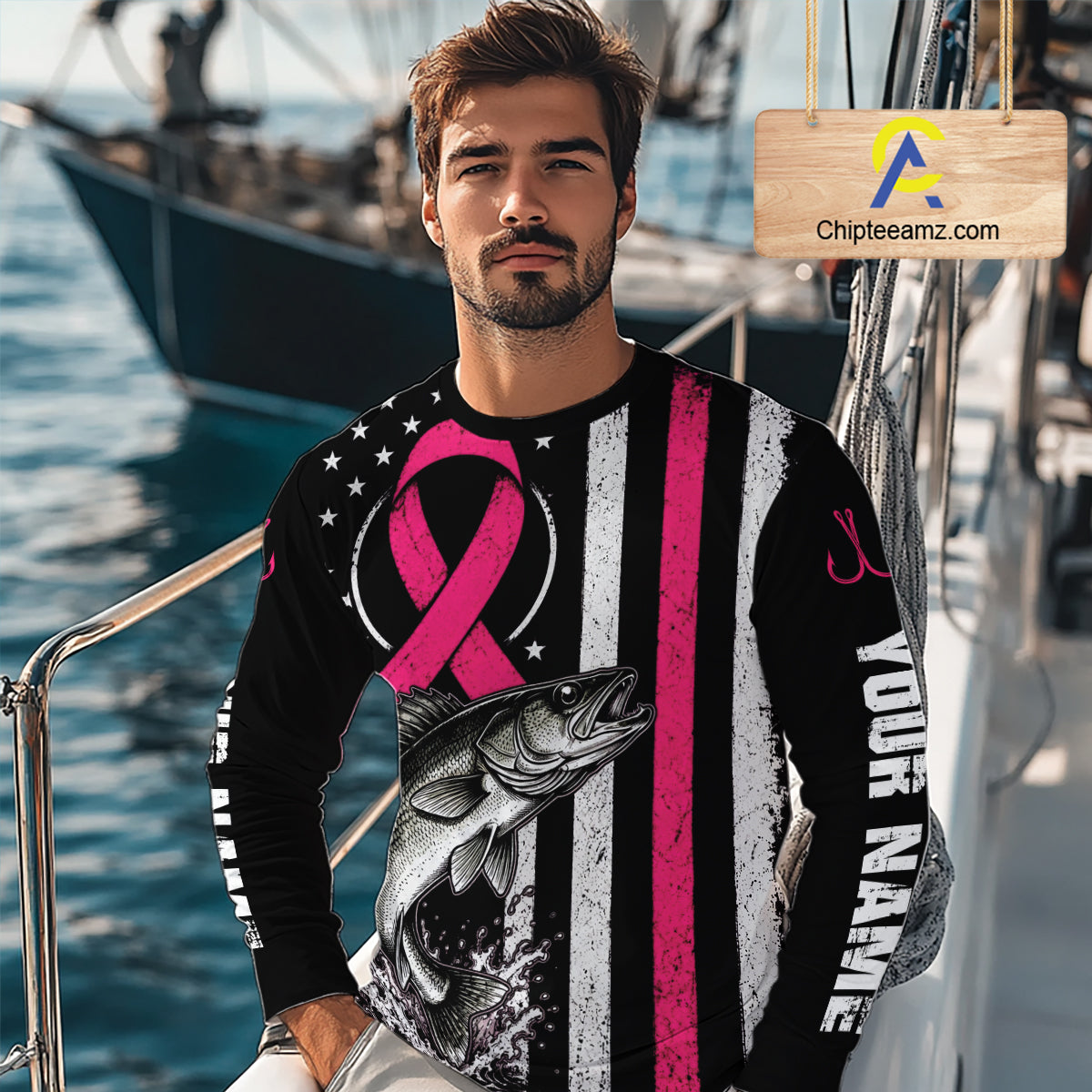 A man wearing a long-sleeve custom graphic shirt on a boat deck, featuring a black and white striped design with a pink ribbon, a fish graphic, and 'YOUR NAME' printed vertically.

